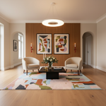 A modern living room interior with two cream armchairs facing a black coffee table on a multicolor abstract-patterned rug. A wood slat accent wall behind the chairs holds two framed abstract paintings, with a ring pendant light overhead and light wood flooring.