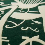 Close-up of a dark green and off-white patterned textile, showing a raised decorative motif with a small black stitched accent.