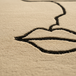 Close-up of a beige textured surface with a black embroidered line drawing of lips and part of a face.