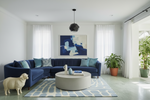 Modern living room with a blue sectional sofa, round coffee table, and abstract blue rug, art on the wall.