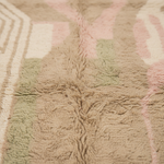 Close-up of a soft, textured area rug with a geometric pattern in beige, dusty pink, and sage green.