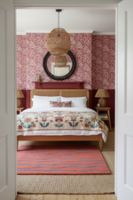 Bedroom with floral wallpaper, wooden bed, and decorative rug.