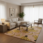 A modern living room featuring a beige sectional sofa, a dark wood coffee table, a light gray armchair, and a large area rug with a yellow banana print on a beige background. The room has warm neutral walls, sheer white curtains, and a potted plant in the corner.