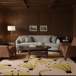 A styled living room with a light gray sofa, two brown armchairs, a round wooden coffee table, and a large patterned area rug in beige, yellow, and black. The room features dark wood paneled walls and a coffered ceiling.