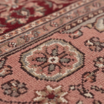 Close-up of a traditional patterned rug with a dusty pink field, a central medallion in muted red, beige, and gray, and a decorative border.