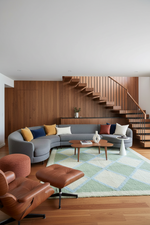 Modern living room with a sectional sofa, coffee table, moroccan  checker shag rug, and staircase in the background.