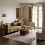 A beautifully styled living room featuring a sage green sofa, a pink and blue patterned area rug, a wooden coffee table, a beige armchair, and floral curtains by white French doors.