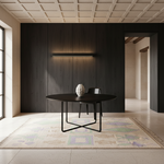 A minimalist dining setup in a modern interior, featuring a round black table with a sculptural black metal base, a black chair, and a textured white vase on a patterned beige rug against a dark wood-paneled wall.