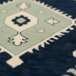 Close-up of a patterned rug showing a pale sage green field with cream geometric motifs and a dark navy border.