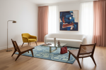 Modern living room with a white sofa, yellow chair, wooden chairs, and abstract art on the wall.