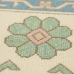 Close-up of a woven textile pattern featuring a large pale green flower with a pink diamond center on a cream background.