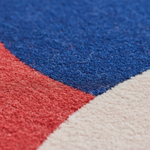 Close-up of a textured rug with a geometric color-block pattern in royal blue, coral red, and cream.