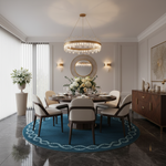A luxury dining room featuring a round dark wood dining table surrounded by six cream upholstered chairs with dark wood frames, set on a blue patterned round rug. The room is decorated with a gold crystal chandelier, a matching round wall mirror, a dark wood sideboard, and a large potted plant.