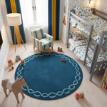 A round dark blue children's rug with a light blue rope border is shown in a styled children's bedroom. The room features a gray wooden bunk bed with yellow and blue patterned bedding, a striped armchair, a wooden toy horse, and a tripod floor lamp.