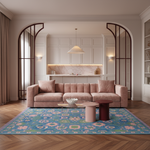A styled living room featuring a dusty pink tufted sofa placed on a large blue and pink patterned area rug. The room has light wood herringbone flooring, a marble backsplash, and arched glass-paneled doorways.