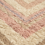 Close-up of a textured, shaggy rug with a chevron pattern in soft cream, dusty pink, and beige tones.