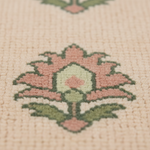 Close-up of a woven textile with a floral motif in dusty pink, sage green, and cream on a warm beige background.