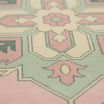 Close-up of a patterned rug with a geometric design in soft pink, sage green, cream, and dark green.