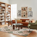 A styled living room interior with a terracotta orange sofa, green armchair, round coffee table, patterned rug, bookshelves, and framed wall art. No person or animal is present, but this is still not a clean isolated product shot; it shows the furniture in a real room setting, so subject_type is Lifestyle.