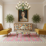 A styled interior scene with a pink patterned area rug, two mustard yellow armchairs, a matching patterned coffee table, a colorful geometric sideboard, potted trees, and a framed portrait on the wall. The room is brightly lit and symmetrical.
