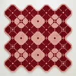 A square textile rug or mat with a geometric pattern in deep burgundy red and light pink, shown flat against a plain off-white background.