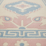 Close-up of a patterned rug with a cream base and raised motifs in soft pink and light blue, including a central medallion, floral details, and a Greek key border.
