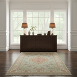 A traditional area rug with a floral medallion pattern in beige, pink, and blue, styled on a dark wood floor in a bright, classic room with a dark wood credenza and lamps.