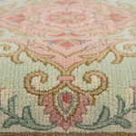 Close-up of a plush area rug with an ornate traditional pattern in soft pink, beige, sage green, and cream.