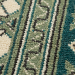 Close-up of a patterned rug showing vertical stripes with cream, sage green, teal blue, and black woven details.