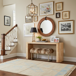 Staircase with wooden handrail, round mirror, beige runner rug, and decorative items on a console table.