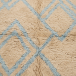 Close-up of a textured rug with a beige shaggy surface and a light blue geometric diamond pattern.