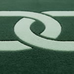 Close-up of a dark green textured surface with a large pale green abstract curved logo or emblem.