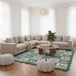 A styled living room featuring a light beige sectional sofa, a green and cream patterned scalloped area rug, a round wooden coffee table, two white knit pumpkin ottomans, and a potted green plant.