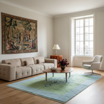 A modern living room featuring a beige tufted sofa, a light green and blue area rug, a round wooden coffee table with a vase of flowers, a white swivel armchair, and a large classical-style tapestry on the wall.