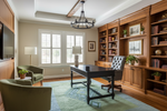 Home office with wooden desk, bookshelves, and armchairs.