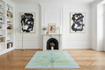 Modern living room with yellow sofa, blue green shag rug, abstract art, and a fireplace.