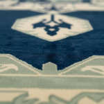 Close-up of a patterned rug with a deep blue field, cream geometric medallion motifs, and pale sage green border details.