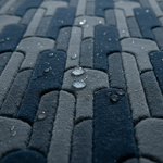 Close-up of a textured, interlocking tufted surface in layered blue-gray and navy tones, with water droplets resting on the top.