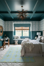 Modern bedroom with teal walls, blue rug, a bed, and decorative elements.