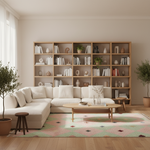 A modern living room featuring a large beige sectional sofa, a light wood coffee table, a patterned pink and green rug, and a tall wooden bookshelf filled with books and decor in the background.