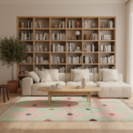 A styled living room featuring a large light wood modular bookshelf filled with books, a cream sectional sofa, a light wood coffee table, a multicolor geometric area rug, and a potted tree.