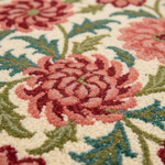 Close-up of a floral area rug with a raised tufted texture, featuring large pink and red flowers with green and teal leaves on an off-white background.