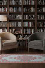 A cozy reading nook with two plush armchairs facing a small wooden side table, set against a backdrop of tall dark wood bookshelves filled with books. A patterned rug is visible on the floor.