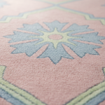 Close-up of a textured area rug with a dusty pink field, a large light blue floral medallion, and pale yellow geometric accents.