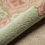 Close-up of a folded area rug showing its plush, textured pile and a traditional floral pattern in dusty pink, sage green, and beige.