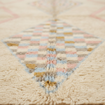 Close-up of a textured rug with a cream base and a central diamond pattern in pastel pink, blue, beige, and mustard yellow.