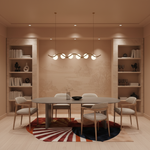 A modern dining room featuring a round dark wood dining table surrounded by six upholstered chairs, under a multi-light linear pendant chandelier. The room is styled with warm beige walls, built-in bookshelves, and a distinctive circular rug with a sunburst pattern.