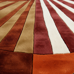 Close-up of a plush area rug with a striped sunburst pattern in rust orange, tan, burgundy, and cream.