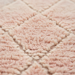 Close-up of a soft, plush rug with a diamond pattern in pale blush pink and cream.