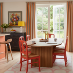 Dining room with round wooden table and red chairs, gray rug, large window, and pink accents.